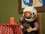 a girl at a table wearing an astronaut helmet and petting a cat on her lap.