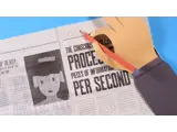 A still image from a stop motion animation. Showing a papercrafted hand , holding a pencil and drawing on a newspaper.